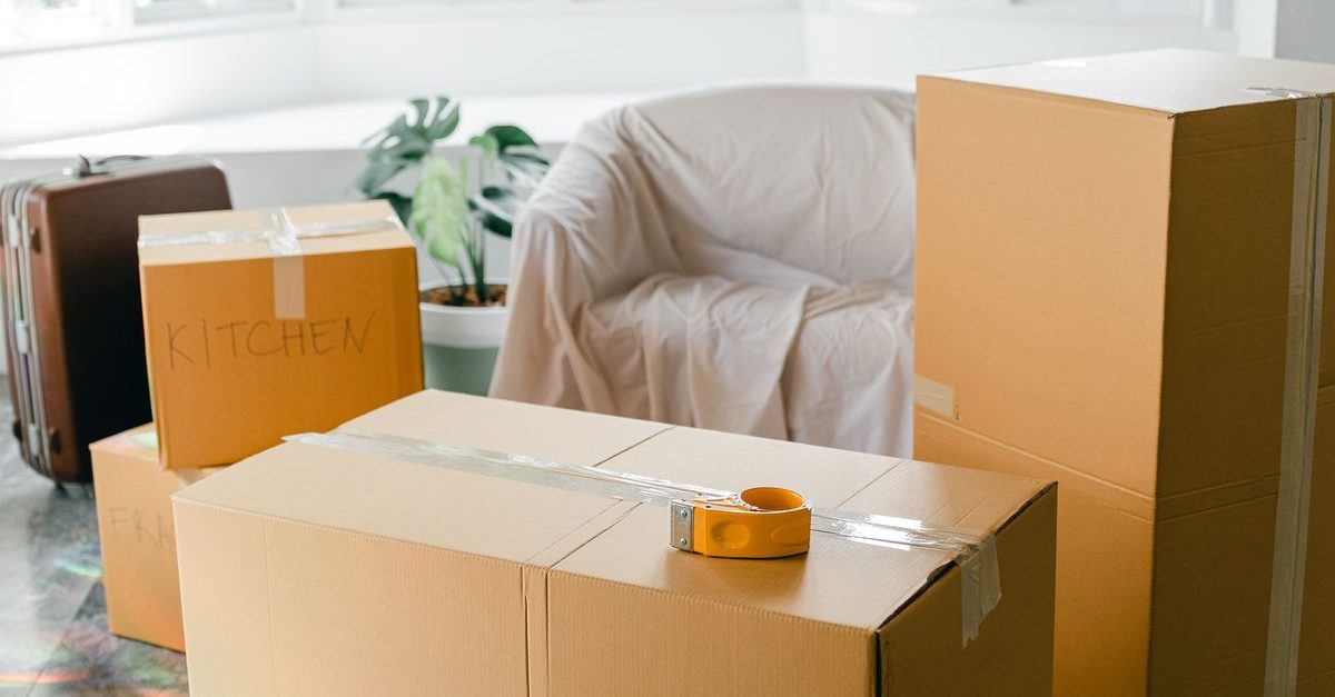 Stacked cardboard moving boxes on a floor inside an empty home with sunlight through large windows