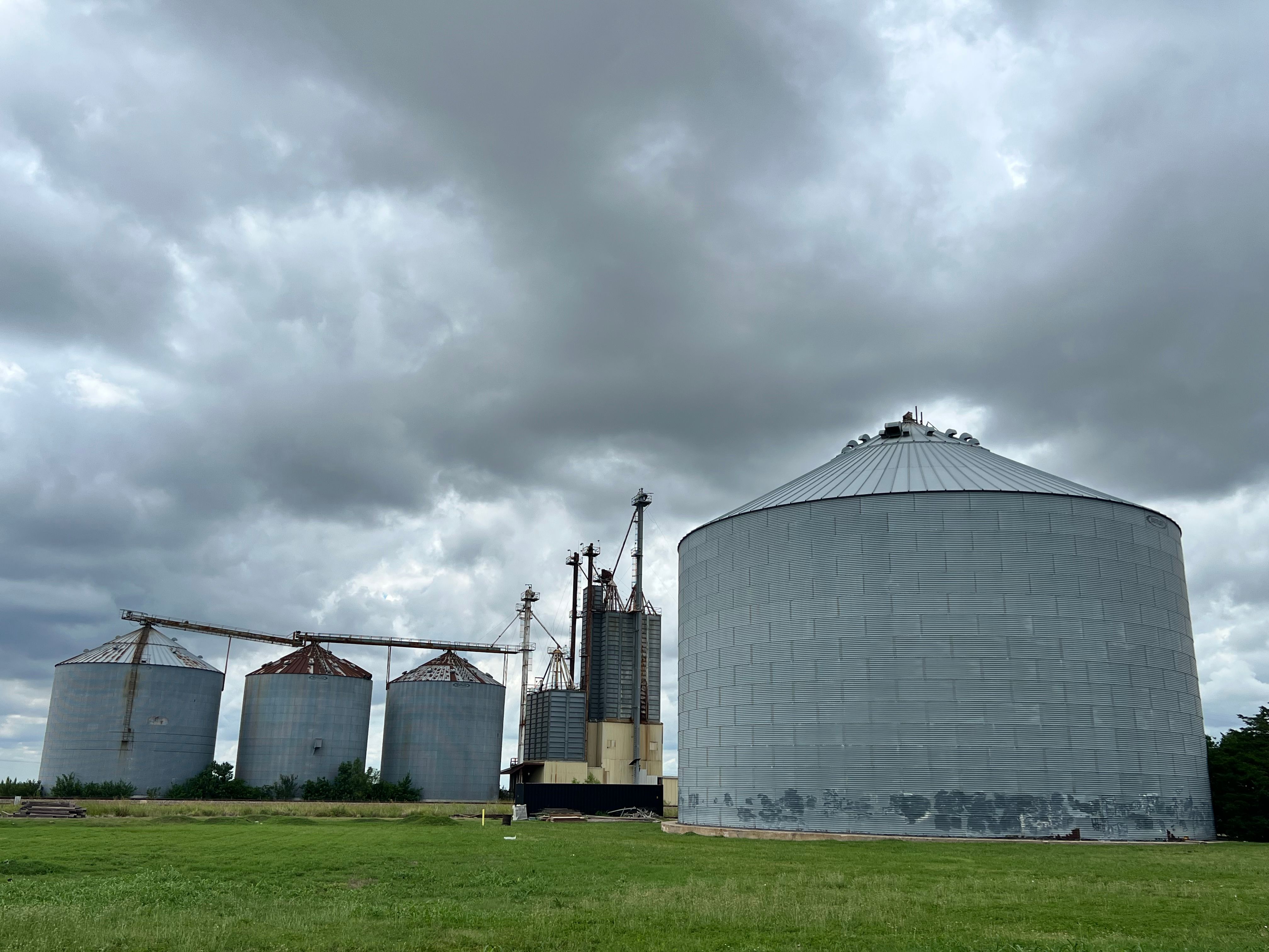 Large grain silos in a rural Texas landscape with overcast skies, showcasing agricultural infrastructure and land in productive use