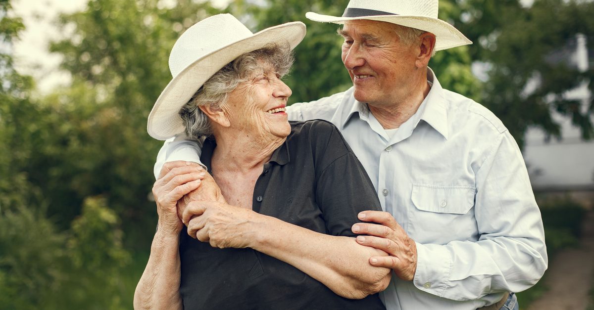 Happy senior couple wearing fedoras, sharing a joyful moment outdoors