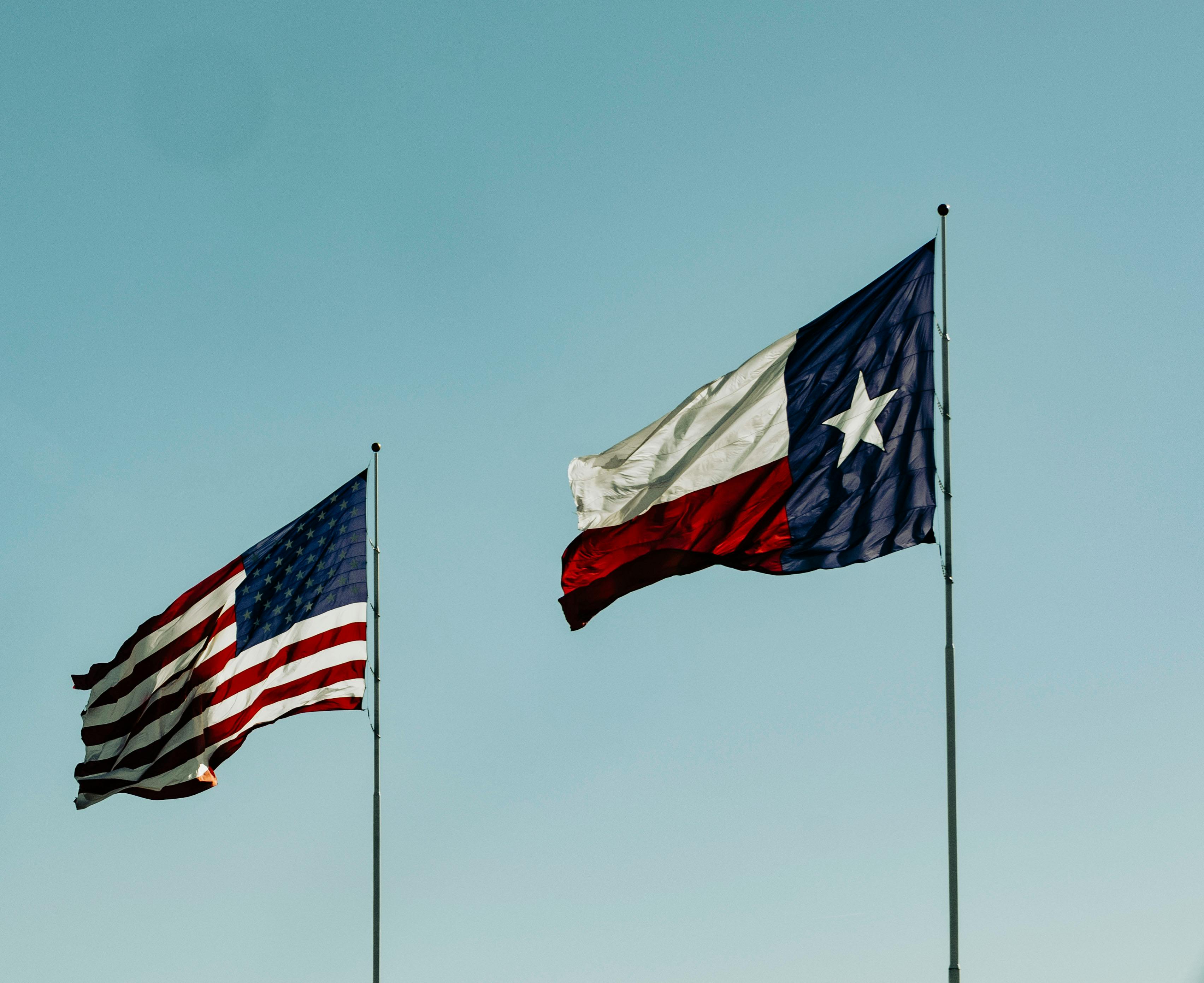 American and Texas flags waving together under a clear blue sky, symbolizing patriotism and the Lone Star State